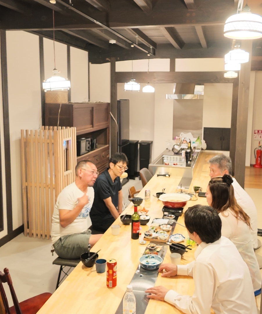 梁のある部屋で、長いテーブルを囲んで食事をする人たち